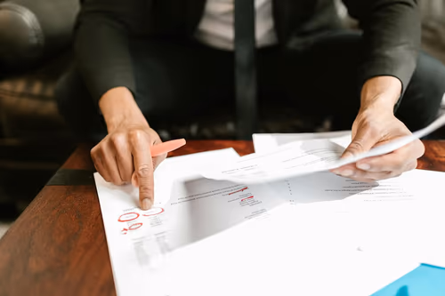 Hands reviewing financial statements with red marker annotations